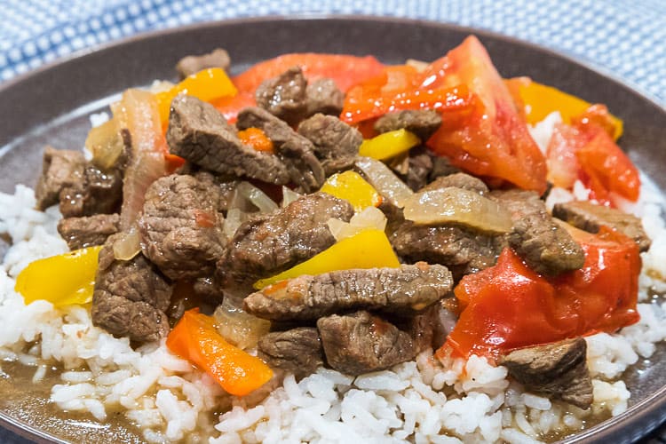 Pepper steak with onions and tomatoes on a bed of white rice.