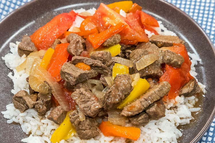 Pepper steak recipe with onions and tomatoes on a bed of white rice.