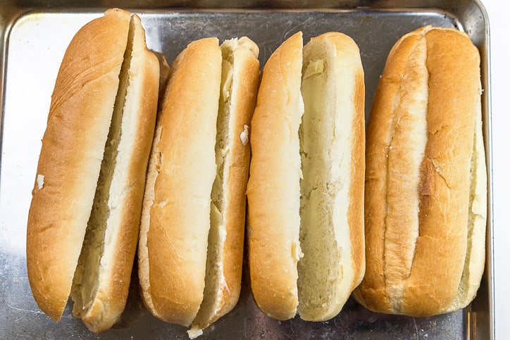 Buttered hoagie rolls on a toaster oven pan.