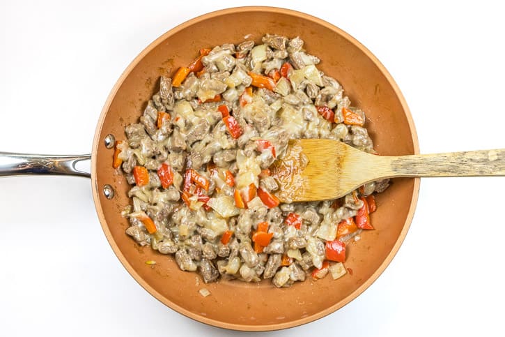 Melted Provolone cheese, steak, onions, and red bell peppers in a frying pan.
