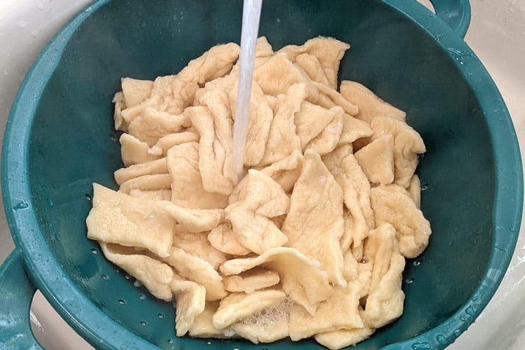 Rinsing the pierogi dumplings under cold water.