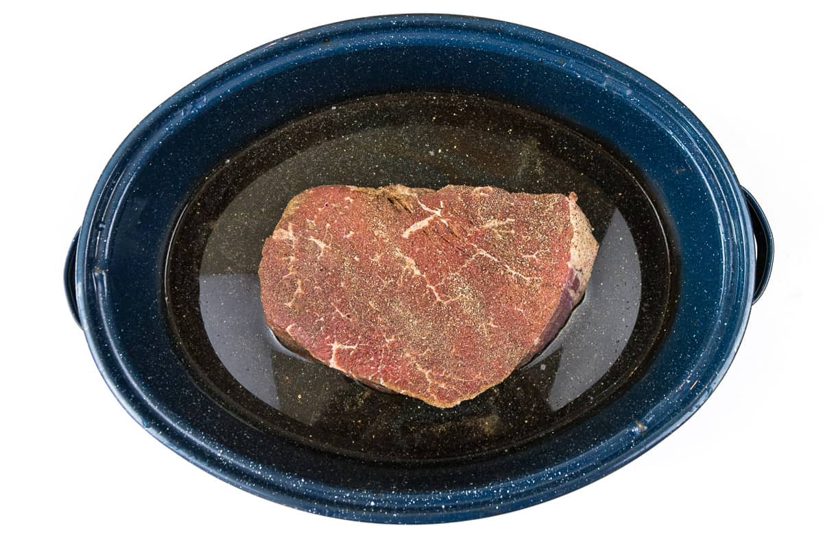 Seasoned pot roast in a roasting pan with water.