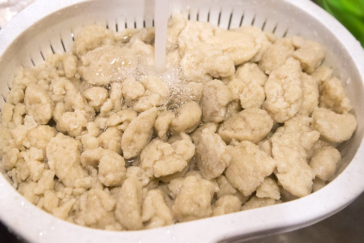 Potato dumplings in colander rinsing under cold water.