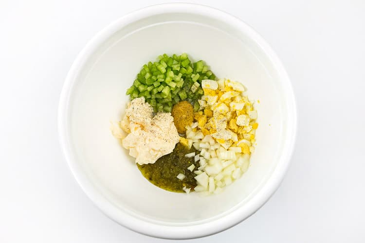 Hard-boiled eggs, celery, chopped onion, sweet relish, salt, pepper, mayonnaise, and yellow mustard in a bowl.