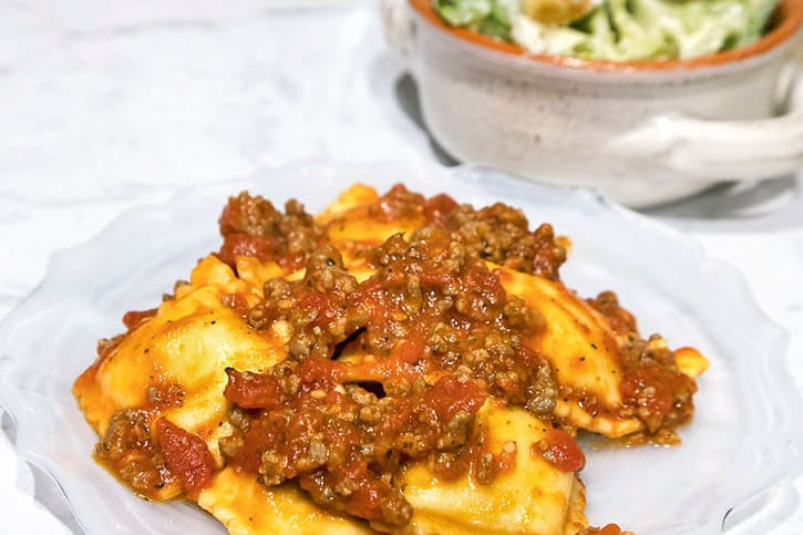 A plate of sausage pasta sauce and five cheese ravioli.