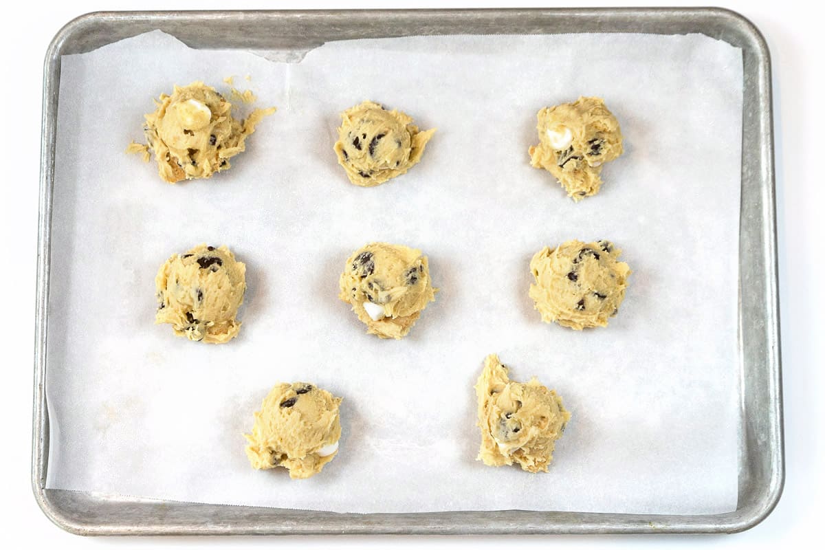 Eight unbaked cookies on a cookie sheet with parchment paper.