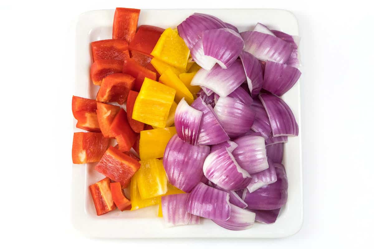 Red bell pepper, yellow bell pepper, and red onion are cut into one-inch squares.