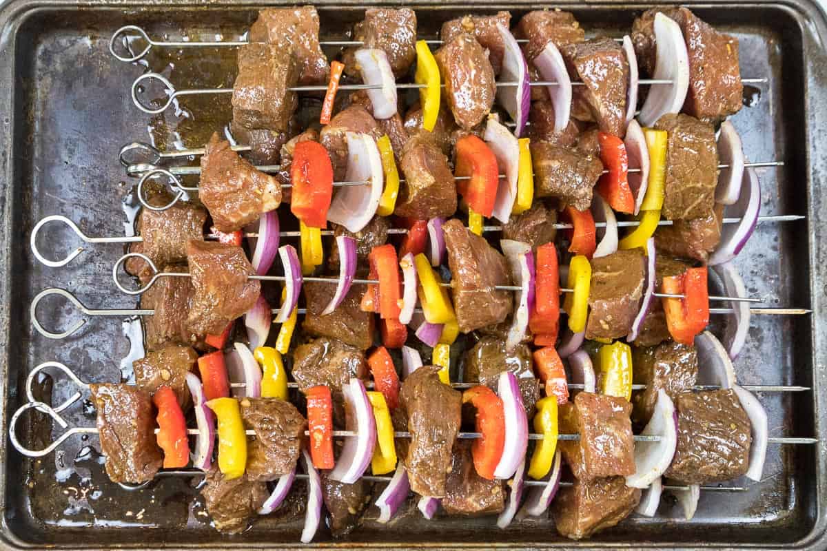 Steak, red onions, red bell peppers, and yellow bell peppers are arranged on the skewers.