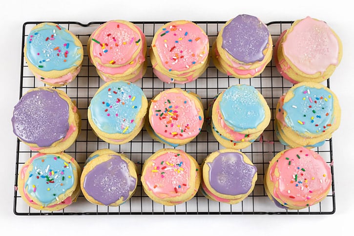 Sugar cookies with icing and sprinkles on a cooling rack.