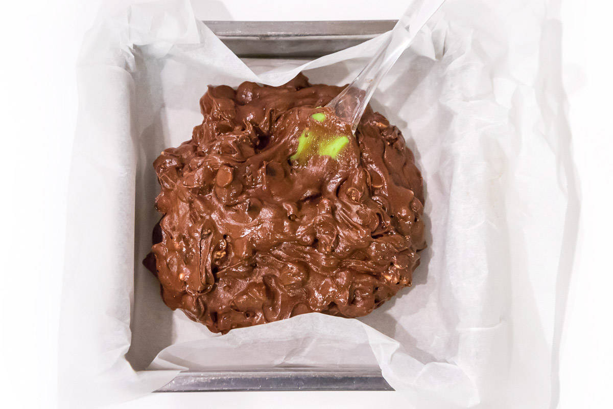 Brownie batter in a nine by nine inch baking pan lined with parchment paper.
